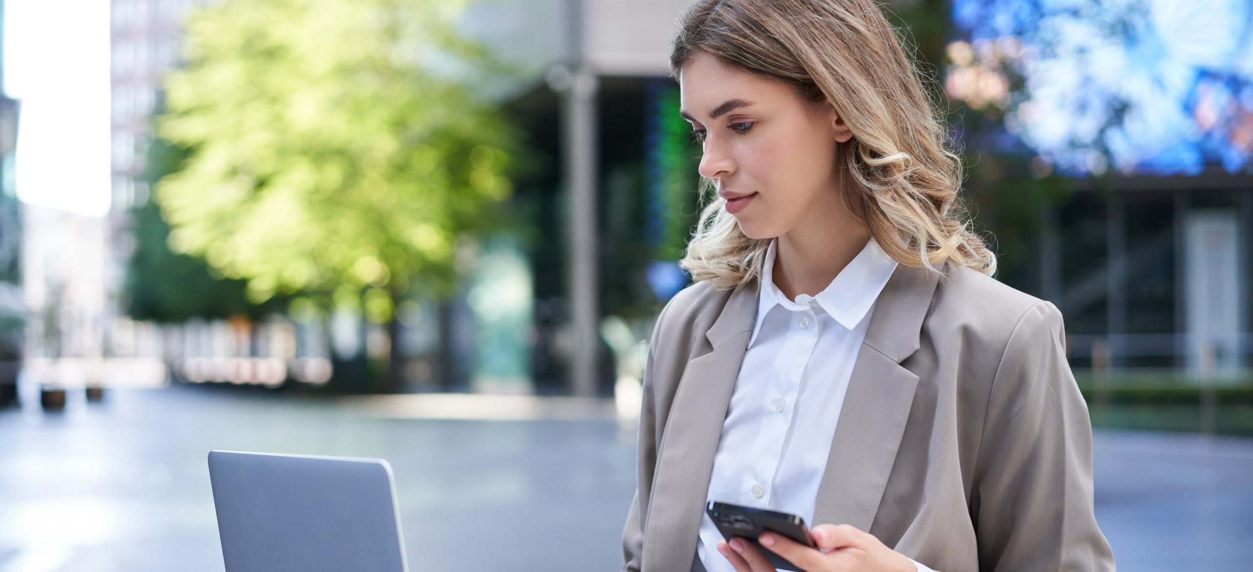 Corporate woman in suit working in city centre, using laptop and mobile phone